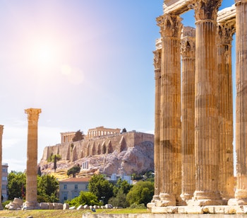 Historiske ruiner af Zeus-templet med udsigt til Akropolis i Athen. Imponerende marmorsøjler fra antikkens Grækenland under en klar blå himmel.