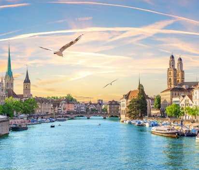 Luftpanorama over Zürichs bymidte ved aftentid med Limmat-floden, Grossmünster og Fraumünster kirkerne omkranset af Schweiz' smukke alper